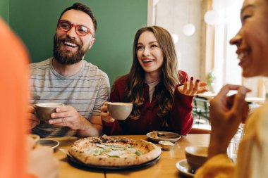 Dört mutlu arkadaş bir restoranda lezzetli bir pizza ve kahve paylaşıyor, birlikte gülüyor ve sohbet ediyor, sıcak ve dostane bir atmosfer yaratıyorlar. İletişim konsepti