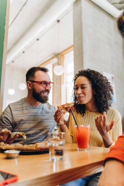 Neşeli erkek ve kadın modern bir pizzacıda keyifli bir öğle yemeği molası veriyorlar, lezzetli pizzanın tadını çıkarıyorlar ve birbirinin dostluğunun ve sohbetinin tadını çıkarıyorlar.