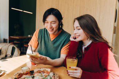 Neşeli çift restoranda bir masada oturmuş pizza ve içkileri paylaşırken, adam akıllı telefonuyla kadınlara komik bir şey gösteriyor. İlişki kavramı