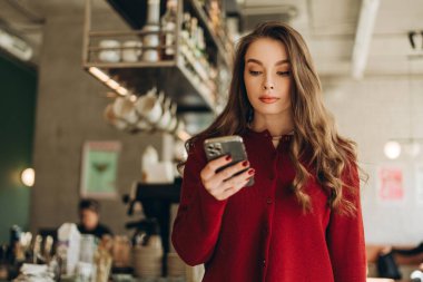 Modern kahve dükkanında akıllı telefon kullanan genç, güzel, ciddi bir kadın. Çevrimiçi alışveriş kavramı