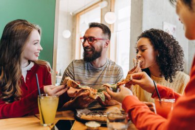 Dört mutlu arkadaş lezzetli pizza dilimlerini paylaşıyor ve serinletici meşrubatlar içiyor, birlikte restoranda kaliteli vakit geçiriyorlar, kahkahalar ve neşeli sohbetlerle dolu. Yiyecek, iletişim konsepti