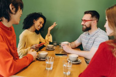Çeşitli uluslar arası arkadaşlar kafe masasında oturup kahvelerini yudumluyor ve canlı sohbetler yapıyorlar. Kahkaha ve bağlantılarla dolu sıcak ve davetkar bir atmosfer yaratıyorlar.