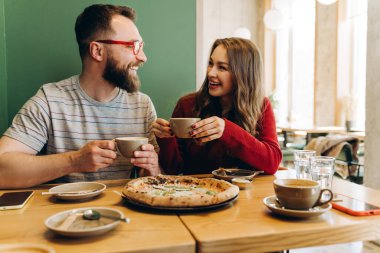 Neşeli erkek ve kadın birlikte hoş vakit geçiriyorlar, modern bir restoranda gündelik bir yemek sırasında lezzetli bir pizza ve kahve paylaşıyorlar. Randevu konsepti