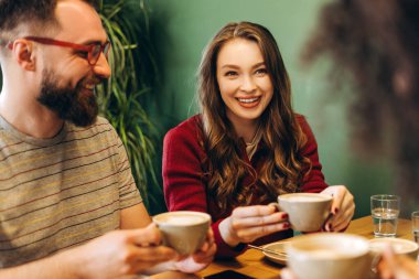 Sıcak bir kafede cappuccinoların tadını çıkarırken gülen ve sohbet eden mutlu arkadaşlar, kahkaha ve bağlantılarla dolu sıcak ve davetkar bir atmosferi teşvik ediyorlar. Rahatlatıcı kavram