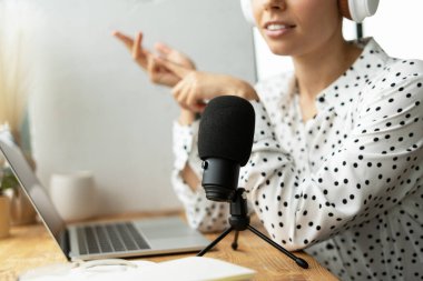 Kulaklık takan içerik yaratıcısı, ses içeriğini konuşurken elleriyle işaret eden profesyonel bir mikrofon ve dizüstü bilgisayar kullanarak kaydediyor. Çevrimiçi podcast kavramı