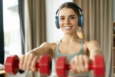Mutlu atlet, spor yaparken dambıllarla egzersiz yapıyor ve evde kulaklıkla müzik dinliyor, sağlıklı yaşam tarzını destekliyor. Eğitim kavramı