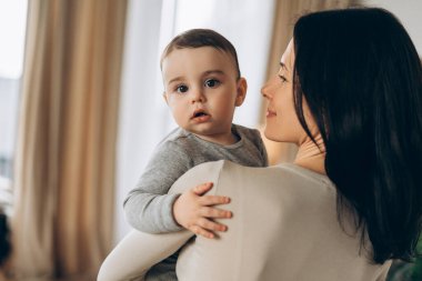 Genç bir anne bebeğini kollarında tutarak, gülümseyerek ve evde birlikte geçirdiğimiz değerli zamanlardan zevk alarak, aile bağlarının iç açıcı bir sahnesini oluşturuyor. Çocukluk kavramı