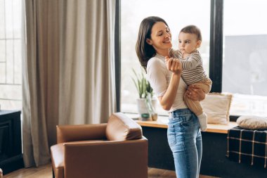 Mutlu anne bebeğini kollarında tutuyor oturma odasında neşeyle dans ediyor ve gülümsüyor anneliğin güzel anlarına ve aile hayatının sıcaklığına değer veriyor. Aile kavramı