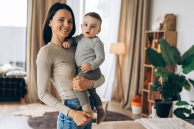 Mutlu anne bebeğini kollarında tutuyor, rahat bir yatak odasında gülümsüyor, aile hayatlarında sevgi ve bağla dolu hassas bir anı kutluyor.