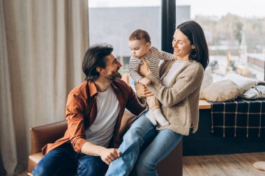 Gülümseyen ebeveynler rahat bir kanepede oturup, küçük oğullarını kucaklar ve davet edilen oturma odalarının sıcak atmosferinde birlikte eğlenceli anların tadını çıkarırlar. Ebeveynlik kavramı