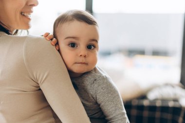 Sevimli bebek evde annesinin omzunda sessizce dinleniyor. Çocuk kameraya bakıyor. Uzayı kopyala Ebeveynlik, aile, aşk ve bakım kavramı
