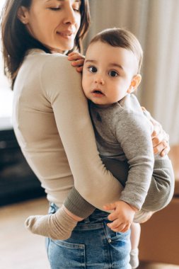 Bebeğini sıcak bir evde kucağında tutan gülümseyen genç bir annenin portresi. Ebeveynlik, aile, aşk ve bakım kavramı