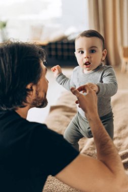 Genç babanın portresi bebek elini nazikçe tutarken çocuk evde rahat bir yatakta duruyordu. Ebeveynlik, aile, aşk ve bakım kavramı