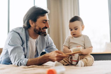 Mutlu baba, bebeği yatak odasındaki krema kavanozunu tutarken fırçayı tutuyor. Ebeveynlik, aile, aşk ve bakım kavramı
