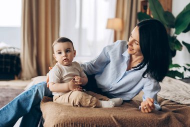 Evde bebeğine bakarken bebeğinin yanında yatan gülümseyen annenin portresi. Ebeveynlik, aile, aşk ve bakım kavramı