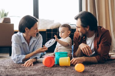 Mutlu genç ebeveynler, evdeki yumuşak halıda birlikte oynayan küçük oğullarına odaklandılar. Ebeveynlik, aile, aşk ve bakım kavramı