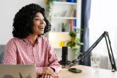 Genç bir kadın mikrofona konuşuyor. Rahat stüdyosundan canlı yayın yapıyor. Mutluluk ve yaratıcılık yayıyor.