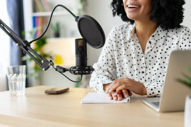 Kadın podcaster, gerekli ekipmanlarla çevrili rahat bir ev stüdyosunda ses yayını yaparken sohbete daldı.