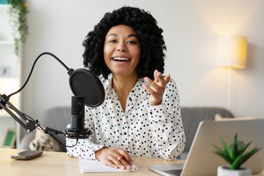 Neşeli kadın podcaster mikrofona konuşuyor ve stüdyosunda ses yayını yapıyor.