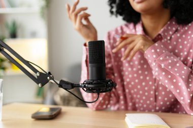 Genç bir kadın, ses içeriğini profesyonel bir mikrofonla kaydediyor. Yaratıcılık sürecinde kendini ifade ediyor.