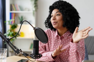 Genç bir kadın stüdyosunda ilgi çekici bir podcast kaydediyor. Seyircileriyle iletişim kurarken coşku ve tutku ifade ediyor.