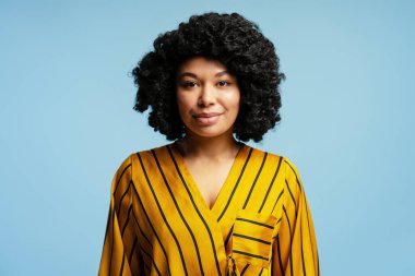 Sarı çizgili bluz giyen kıvırcık saçlı, özgüvenini ve profesyonelliğini ifade eden genç siyahi bir kadının stüdyo portresi.