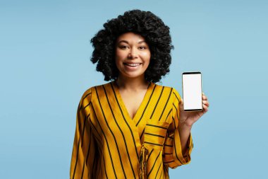 Neşeli iş kadını cep telefonuyla reklam için beyaz ekran sunuyor, mavi stüdyo arka planında izole edilmiş.
