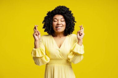 Umut dolu genç bir kadının stüdyo portresi. Şans diliyor, sarı arka planda izole edilmiş.