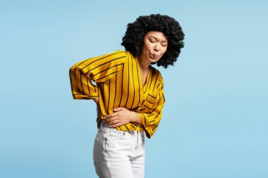 Stüdyo çekimlerinde sırt ve karın ağrısı çeken genç bir kadın sağlık sorunlarını ve rahatsızlığı vurguluyor.