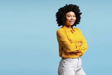 Kollarını kavuşturup gülümseyen genç bir müdürün stüdyo portresi, canlı bir mavi zemine karşı özgüven ve profesyonellik yayıyor.