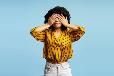 Saçları kıvırcık, elleri açık mavi arka planda olan genç bir kadının stüdyo portresi.