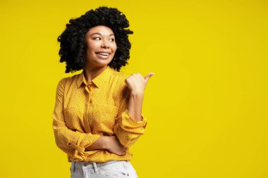 Sarı arka planda gülümseyen kıvırcık saçlı genç bir kadının stüdyo fotoğrafı.