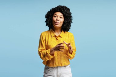 Stüdyoda, sarı tişörtlü, mavi arka planda konuşan Afro-Amerikalı genç bir kadının belden yukarı pozu.
