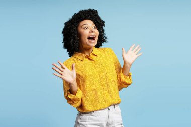 Şaşırmış bir Afrikalı Amerikalı kadının stüdyo portresi. Mavi arka planda tek başına el kaldırıyor ve nefes nefese.
