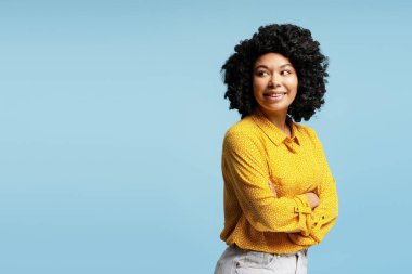 Mavi bir arka planda, kollarını kavuşturup gülümseyen genç bir kadının stüdyo portresi.