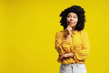 Düşünceli iş kadını kafasını kaldırıyor ve çenesine dokunuyor. Fotokopi çekilen parlak sarı arka planda izole edilmiş.