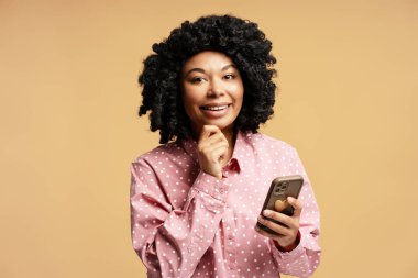 Akıllı bir telefon tutan genç bir kadının portresi. Düşünceli bir şekilde çenesine dokunurken gülümsüyor. Mutluluk saçıyor.