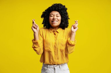 Umut dolu parmakları çapraz genç bir kadının stüdyo portresi. Sarı arka planda iyi şanslar ve olumlu sonuçlar umarak bir dilek tutuyor.