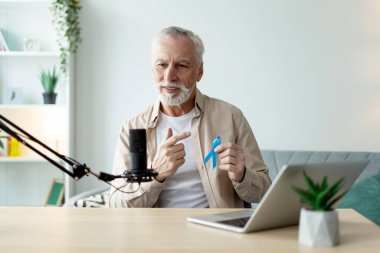 Olgun podcaster canlı yayın sırasında mavi kurdeleyi gösteriyor, prostat kanseri hakkında farkındalığı artırıyor