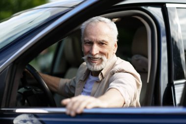 Arabasında oturan, direksiyonu tutan, emekliliğinin tadını çıkaran neşeli bir son sınıf öğrencisinin portresi.
