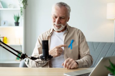 Mavi prostat kanseri farkındalığı kurdelesi takan yaşlı podcaster, erkek sağlığı hakkında podcast bölümü
