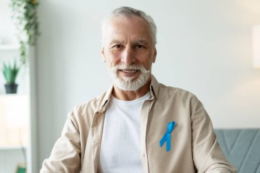 Açık mavi farkındalık kurdelesi takan gülümseyen bir son sınıf öğrencisinin portresi, sağlığı destekliyor ve tıbbi nedenlere destek veriyor.