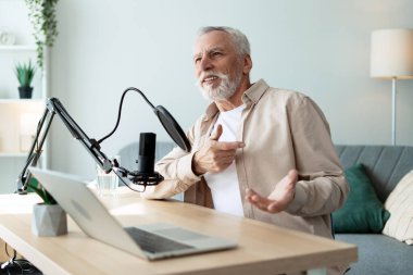 Mutlu, olgun bir adam sohbete daldı ve canlı bir şekilde el kol hareketi yaparak samimi bir ev stüdyosunda podcast çekti.