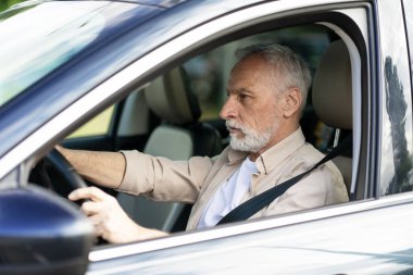 Emniyet kemeri takmış araba kullanan, ilerideki yolda ilerlemeye odaklanmış son sınıf öğrencisi.
