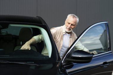 Gülümseyen son sınıf öğrencisi park ettikten sonra şık siyah arabasından iniyor. Mutluluk ve memnuniyet saçıyor.