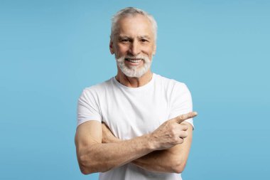 Mavi bir arka planda çapraz kollarla dururken parmağıyla işaret eden neşeli bir kıdemli adamın portresi.