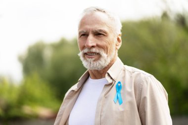 Prostat kanseri için açık mavi farkındalık kurdelesi takan gülümseyen son sınıf öğrencisinin portresi.