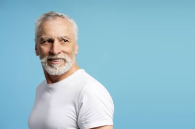 Beyaz sakallı, şık bir son sınıf öğrencisinin portresi. Gülümsüyor ve mavi bir arka plana bakıyor. Kendine güven ve neşe saçıyor.