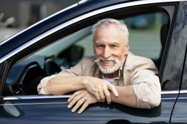 Neşeli kıdemli adam yeni arabasında rahat bir şekilde oturuyor, emekliliğini kucaklıyor ve açık yolların özgürlüğünün tadını çıkarıyor.