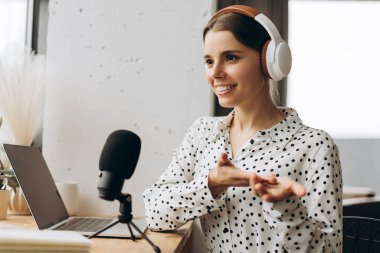 Genç bir kadın stüdyoda mikrofon ve kulaklık kullanarak ses yayını yapıyor. Canlı, çevrimiçi iletişim kavramı